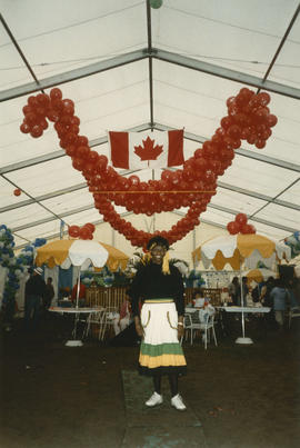 Woman under Canadian flag and decorative balloons inside the Heritage Showcase tent