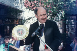 Mike Harcourt holding decorative plate during the reenactment of the first city council meeting a...