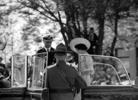 [An R.C.M.P. officer assists King George VI and Queen Elizabeth to get into a car]