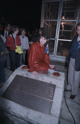 Carole Taylor seated on plaque for Nine O'Clock Gun holding trigger