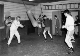 [Men working out in with punching bags and skipping rope]