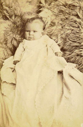 [Studio portrait of baby in christening gown on a fur blanket]