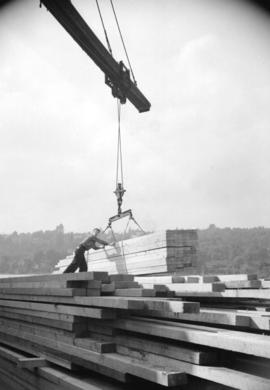 [Man positioning load of lumber being moved by crane]