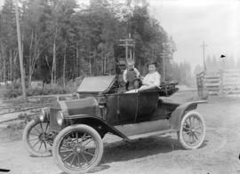 [Man, woman and child seated in car next to railway tracks]