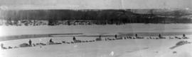 [View of men and dog sleds beside a river]