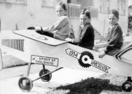 [Three boys sitting on a toy airplane]