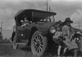 Woman in car with two children sitting on bumper