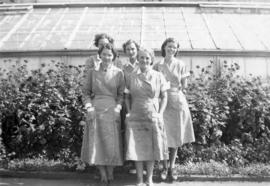 Five women workers posing in uniform dress outside greenhouse