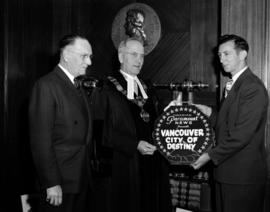 [Mayor Cornett being presented with a "Vancouver, City of Destiny" film reel]