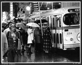 Christmas shoppers [group of people waiting in the rain to board the Victoria bus with people wal...