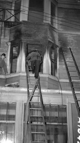 [Firemen on ladders at an upper window of a building]
