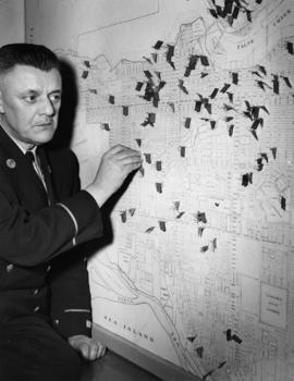 [Chief Fire Warden Louis Mulligan examines map showing arson distribution in the city]