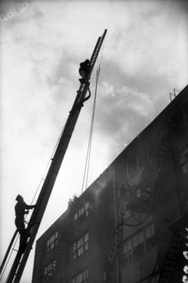 [Firemen on tower ladder wagon at scene of a building fire]