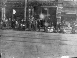 [People lined up in front of Edward Chapman Clothier on the north side of the 600 Block West Hast...