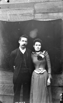 [Man and woman posing in front of sheet placed on exterior of building]