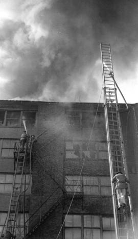 [Firemen on ladders at scene of a building fire]