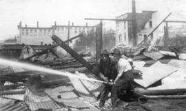 [Two men hosing down the ruins after the fire at Wallace Shipyards]