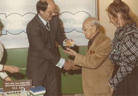 Mike Harcourt handing cake to unidentified man with Kerri Groves beside