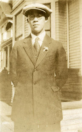 [Young man in suit standing in front of houses]