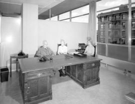 [Major J.S. Matthews, City Archivist, with Mrs. Jean Gibbs and another woman at his desk in the C...