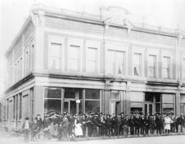 [A group of men and children in front of the Acadia Restaurant at the corner of Abbott Street and...