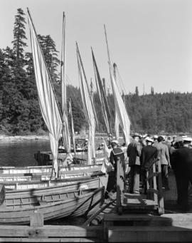 [Naval cadets and other on a dock by a row of wooden sailboats]