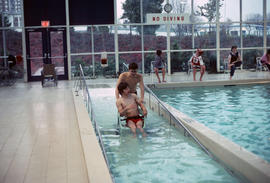 [Boy in wheelchair being pushed down ramp in pool]