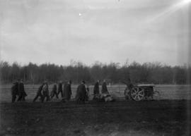 Man on tractor tilling a field with men walking behind