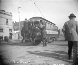[People hanging on to back of streetcar at Hastings and Carrall Streets]