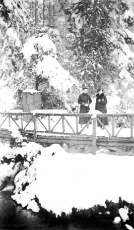 Two women standing on a wooden bridge with lots of snow