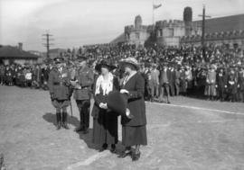 Women standing in front of a group, men in uniform
