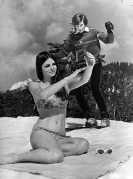 Linda Bindley sun tanning in swimsuit on Grouse Mountain with skier in background