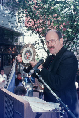 Mike Harcourt holding decorative plate during the reenactment of the first city council meeting a...