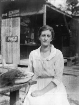 [Woman seated outside at wooden table with bowls of vegetables]