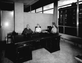 [Major J.S. Matthews, City Archivist, with Mrs. Jean Gibbs and another woman at his desk in the C...