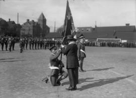 Military officer holding a flag, kneeling in front of a woman
