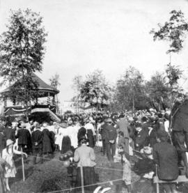 [A crowd around a decorated bandstand]