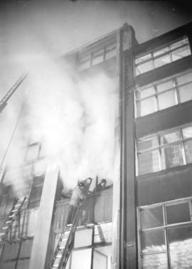 [Firefighters on ladder and inside building fighting fire at the Mainland Building]