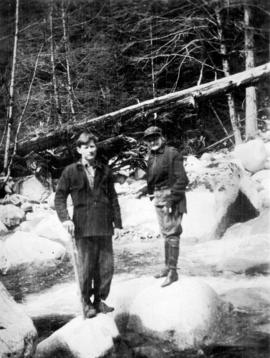 [Unidentified man and woman standing on large rocks in river near Summit Lake]