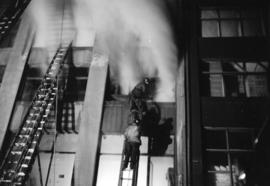 [Firefighters on ladders fighting a fire at the Mainland Building]