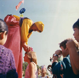 Performer on stilts with children on P.N.E. grounds