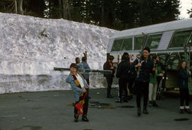 [Kid and adults with skis beside snowbank and bus]