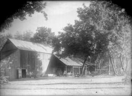 [Farm buildings with carriages stored beside the building under cover]