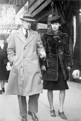 [Unidentified man and woman walking along street]