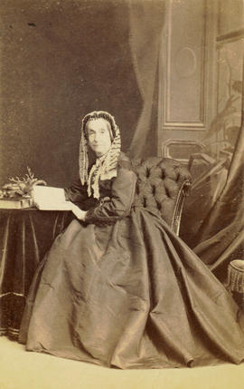[Studio portrait of older woman in lace cap, seated at a table]
