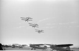 [Bi-planes in flight and airplanes on the ground at airshow]