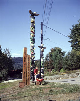 [A couple in front of the totem poles at the entrance to Evergreen Park resort]