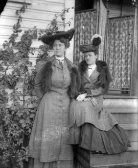 [Two women in hats and furs on front steps]