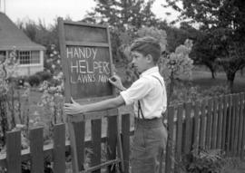 [Young boy making a chalkboard sign offering lawn mowing services]