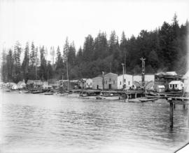 [Builders and totem poles along waterfront at Alert Bay]